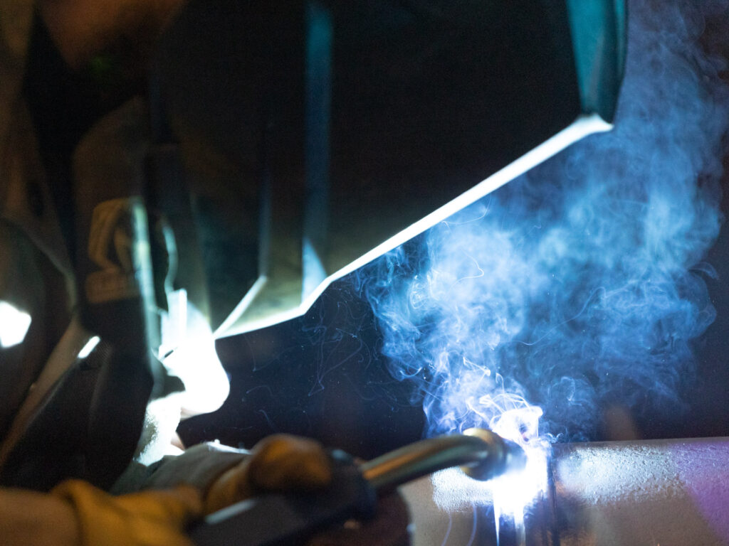 SOR employee welding a pipe while wearing a welding helmet and protective gloves